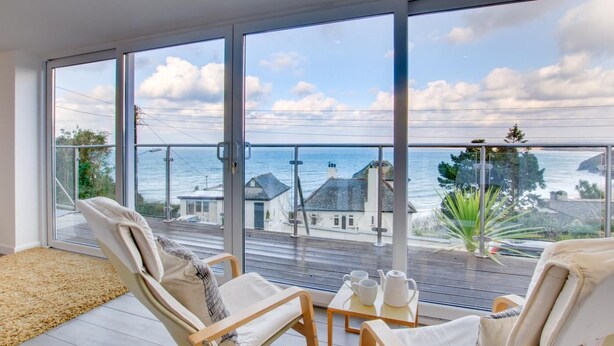 Ein Balkon mit Meerblick, zwei Stühle, ein kleiner Tisch mit Tassen und einem Teekessel, sowie ein Teppich auf dem Boden.