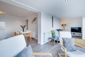 Ein modernes Wohnzimmer mit einer Couch, einem Fernseher und einem Essbereich mit Tisch und Stühlen.
