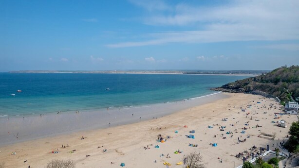Une plage avec des tentes et des gens, un ciel dégagé et une mer calme.