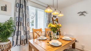 Ein Essbereich mit Holztisch, Stühlen, einer Vase mit Blumen und hängenden Pendelleuchten.
