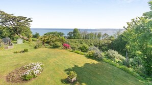 Ein gepflegter Garten mit Rasen, verschiedenen Pflanzen und Blick aufs Meer.