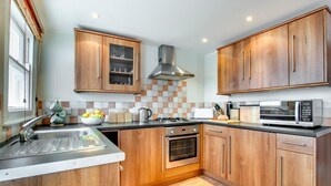 A modern kitchen with wooden cabinets, a stainless steel range hood, a microwave, and a gas stove. - 2 Bed in St Ives (oc-pmho08) (Saint Ives)