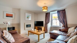 A living room with a TV, sofa, coffee table, fireplace, and artwork on the walls. - 2 Bed in St Ives (oc-pmho08) (Saint Ives)