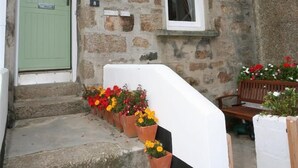 A stone building with a green door, a white window, and a small porch with flower pots. - 2 Bed in St Ives (oc-pmho08) (Saint Ives)