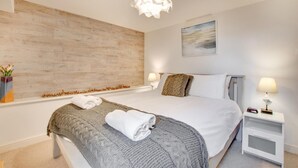 A modern hotel room with a large bed, a wooden accent wall, a painting, and a nightstand with a lamp. - 1 Bed in St Ives (oc-salt3) (Saint Ives)