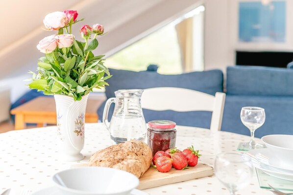 A dining table with a vase of flowers, a pitcher, a jar of jam, bread, strawberries, and a glass of water. - 1 Bed in St Ives (oc-nic48) (Saint Ives)