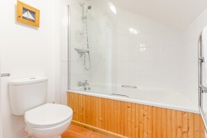 Ein Badezimmer mit Toilette, einer gläsernen Dusche und einer Wand aus Holzpaneelen.
