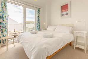 Ein Schlafzimmer mit einem großen Bett, einem Nachttisch, einem Sessel und Meerblick durch ein Fenster.