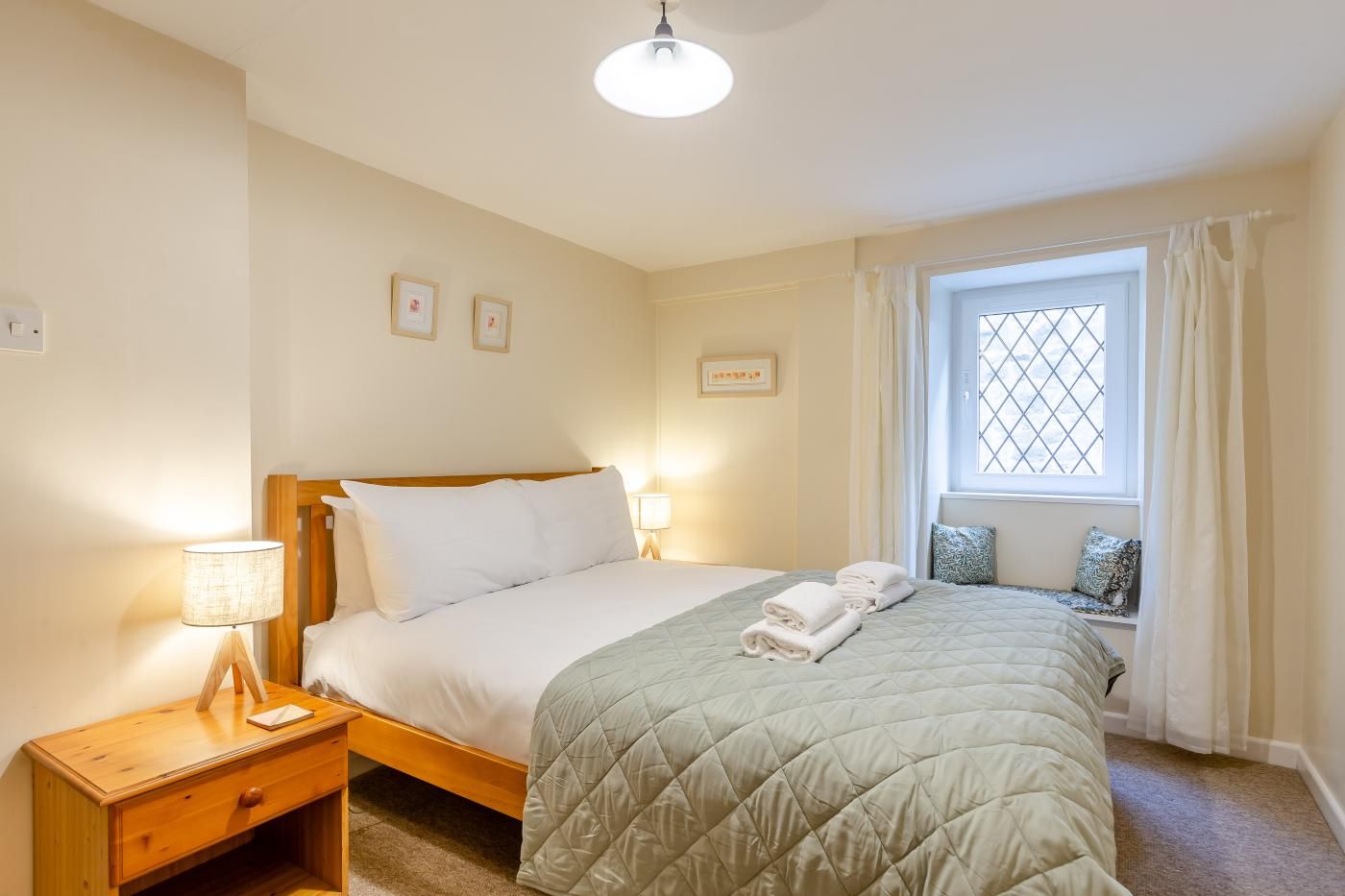 A bedroom with a bed, bedside lamps, a window with curtains, and a small bedside table.