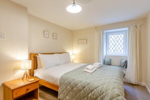 A bedroom with a bed, bedside lamps, a window with curtains, and a small bedside table. - 2 Bed in St Ives (oc-is014a) (St Ives)