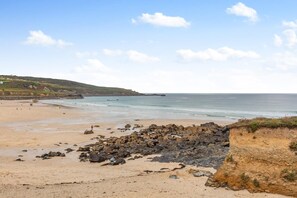 A beach with rocky outcrops, calm sea, and distant hills. - 2 Bed in St Ives (oc-is014a) (St Ives)