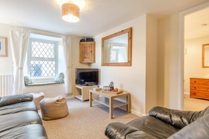 A modern living room with a leather sofa, a television, a coffee table, and a window with curtains. - 2 Bed in St Ives (oc-is014a) (St Ives)