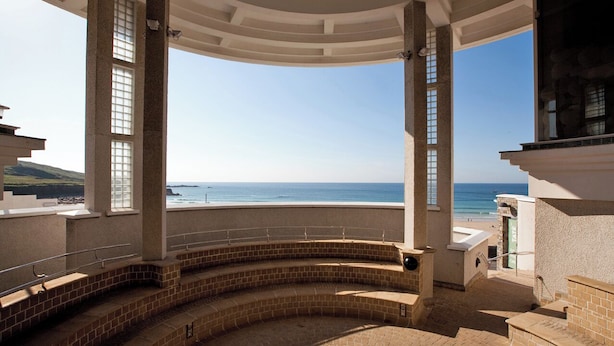 Ein überdachter Außenbereich mit einer gebogenen Ziegelbank, einer Brüstung und Blick auf das Meer.