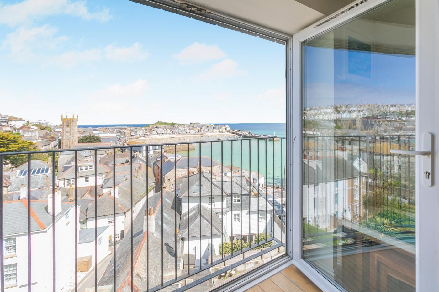 A balcony with a view of a coastal town, a clear sky, and a building with a clock tower.