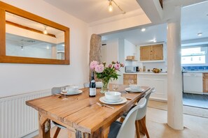 A dining area with a wooden table, white plates, and a wine bottle. - 1 Bed in St Ives (oc-pmap10) (Saint Ives)