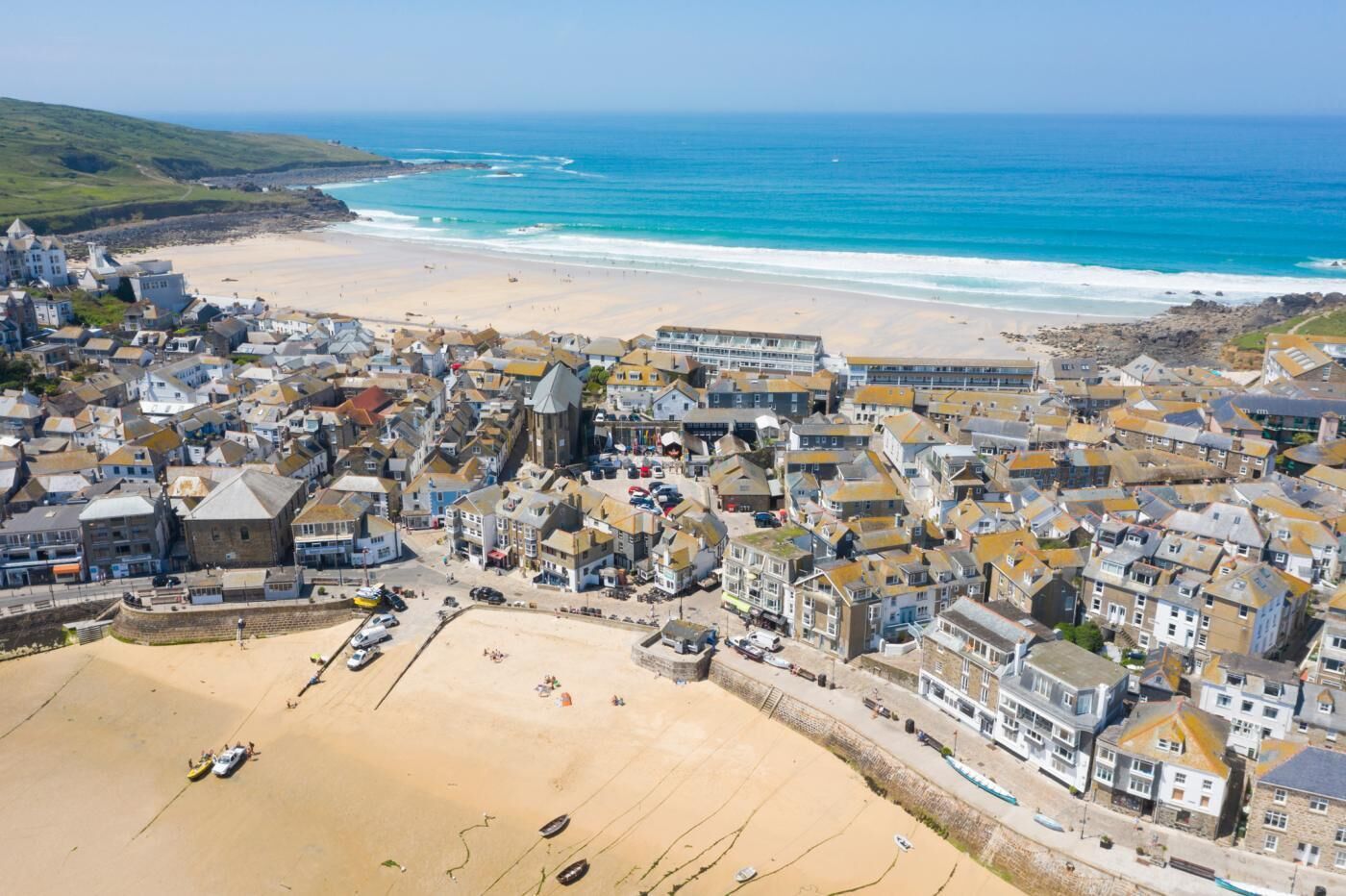 A coastal town with a sandy beach, a mix of residential and commercial buildings, and a clear view of the ocean.
