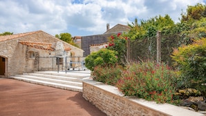 A stone building with a tiled roof, a stone wall, and a garden with red flowers. - Gîte Le Romarin: Shared Pool, Communal Terrace & Wi-Fi in Courçon (Courçon)