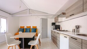 A modern kitchen with a dishwasher, a dining area with a table and chairs, and a view of the outside. - Gîte Le Romarin: Shared Pool, Communal Terrace & Wi-Fi in Courçon (Courçon)