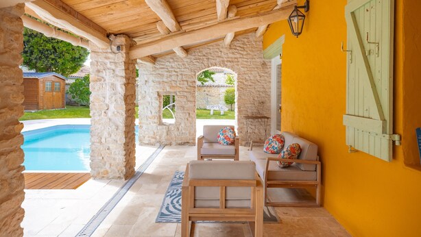 A covered outdoor seating area with stone pillars, a pool, and a yellow wall. - Gîte Le Romarin: Shared Pool, Communal Terrace & Wi-Fi in Courçon (Courçon)
