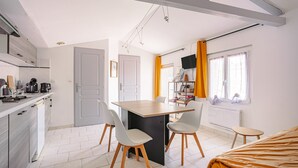 A compact kitchen with modern appliances, a dining area with a central island, and a cozy bed. - Gîte Le Romarin: Shared Pool, Communal Terrace & Wi-Fi in Courçon (Courçon)