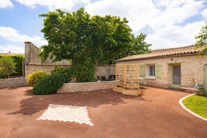 A courtyard with a paved area, a wooden pergola, and a stone building with a tiled roof. - Gîte Le Romarin: Shared Pool, Communal Terrace & Wi-Fi in Courçon (Courçon)