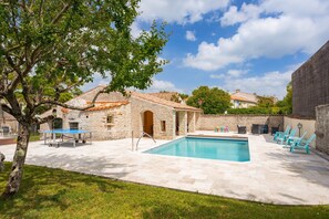 Un edificio de piedra con piscina, mobiliario exterior y un árbol.