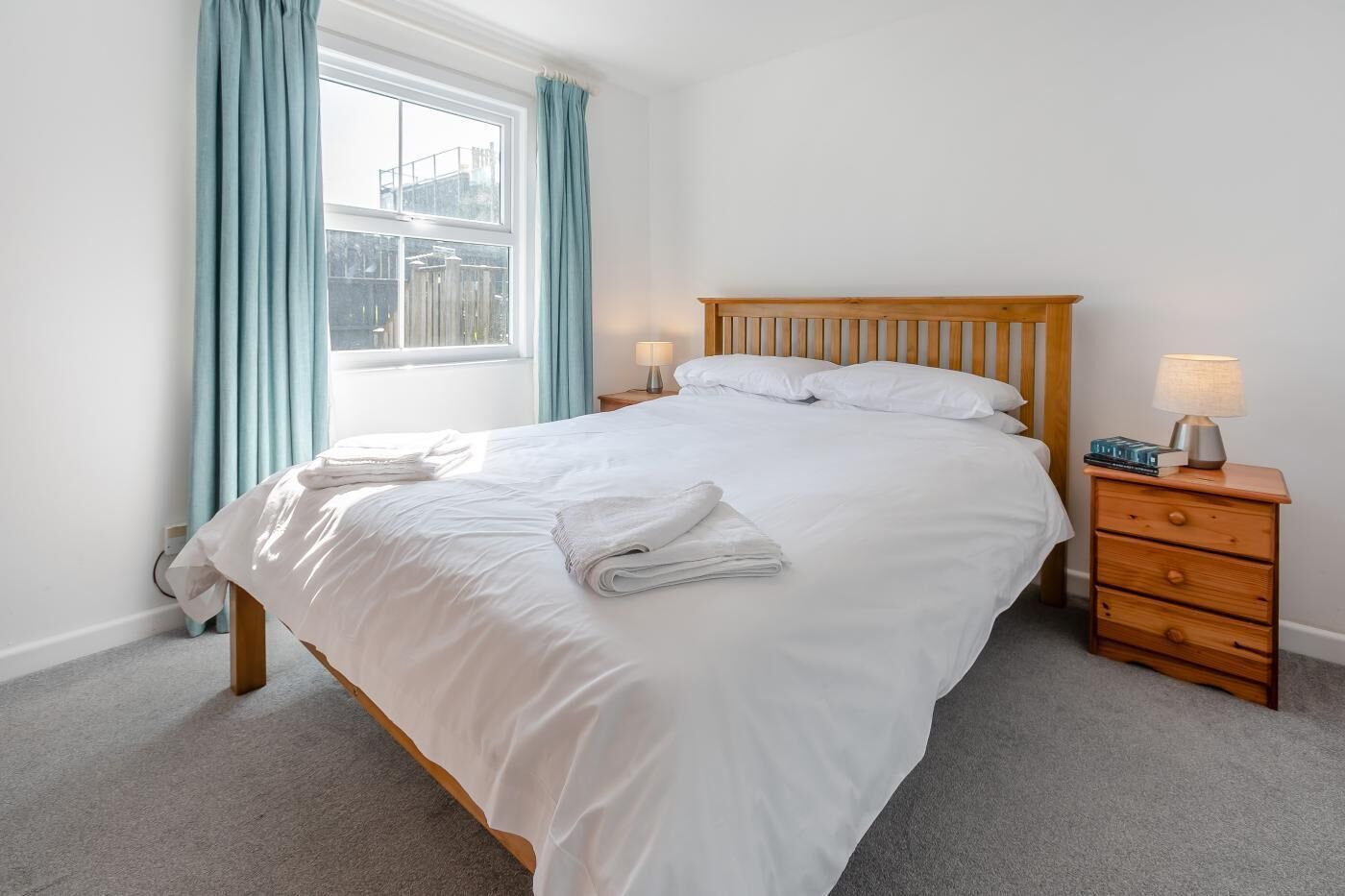 A neatly made bed with white linens, a wooden headboard, and a bedside table with a lamp.