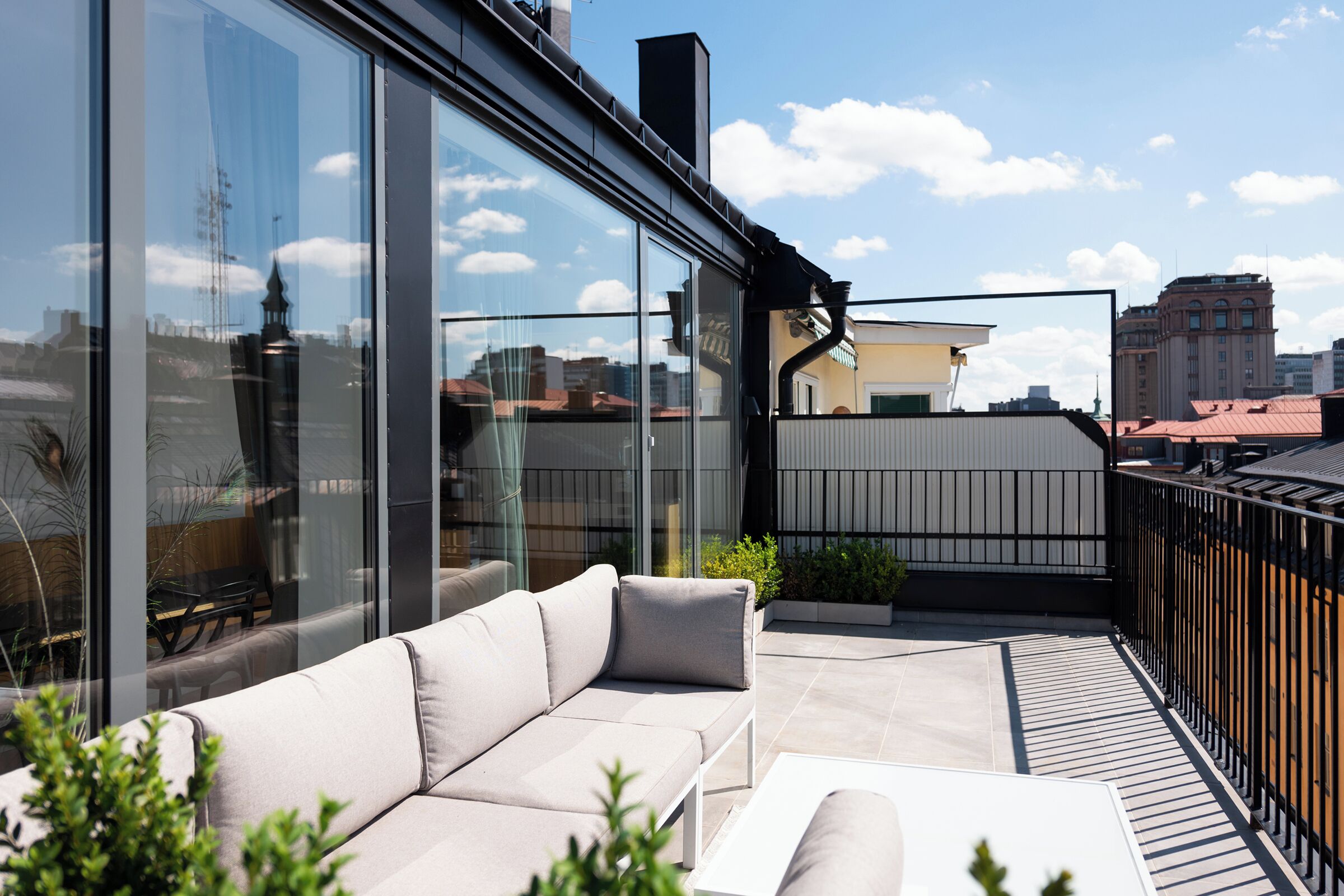 Un espace de vie extérieur moderne, doté d’un canapé, d’une table et d’un mur en verre offrant une vue sur la ville.