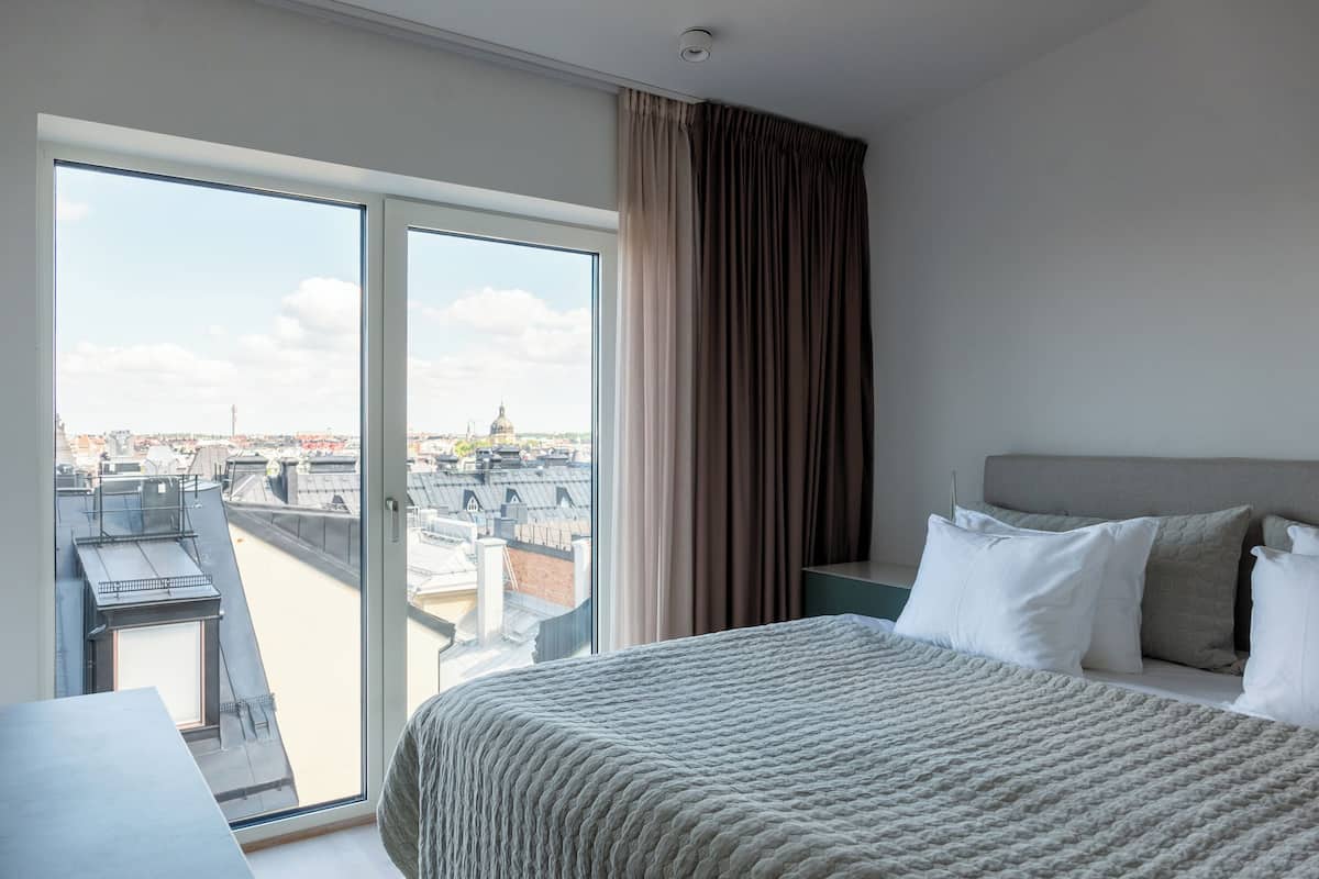 Et hotelværelse med en stor seng, udsigt over bybilledet gennem en skydedør og en balkon med byudsigt.