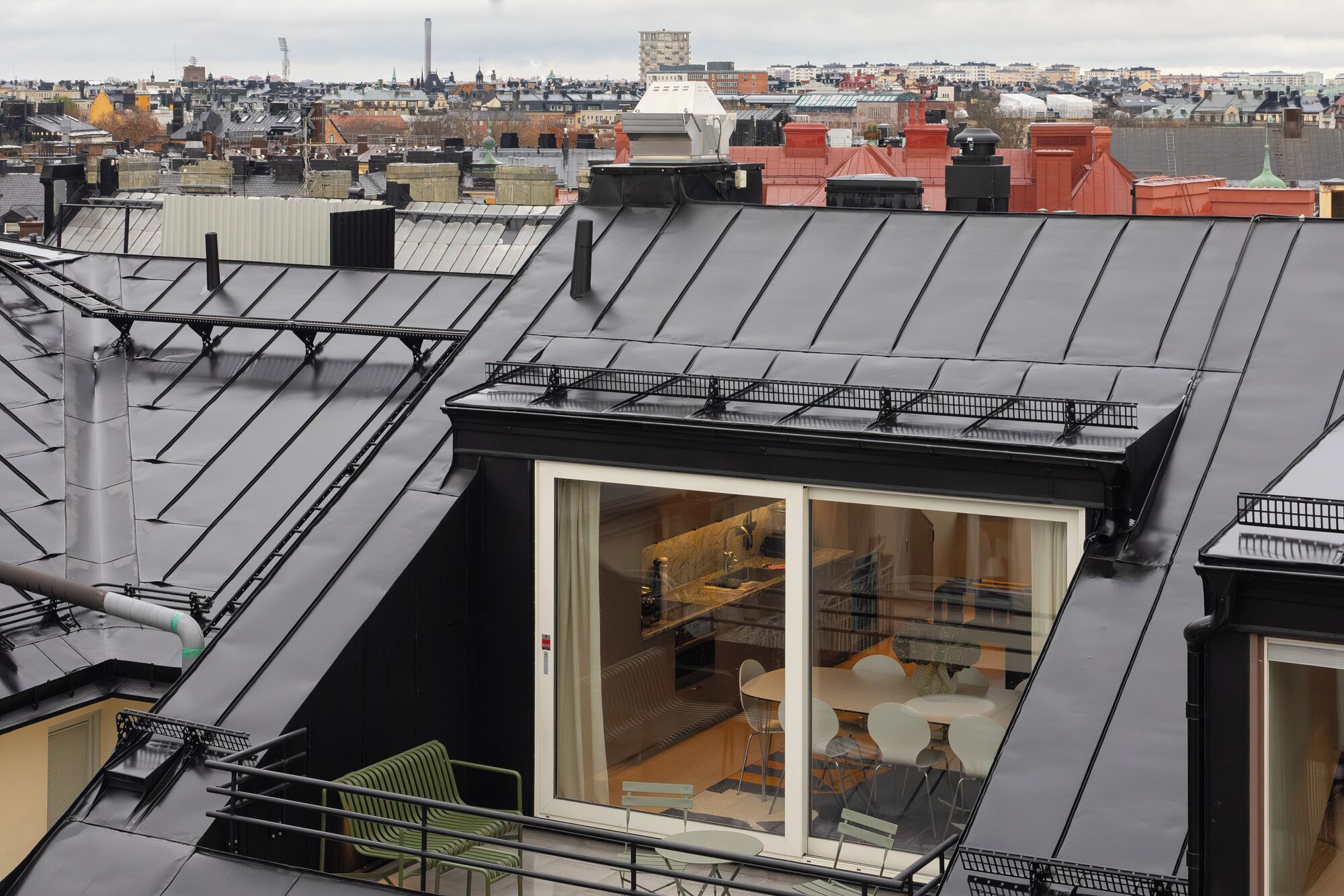 Una terraza en la azotea con cerramiento de vidrio, barandilla metálica y vistas panorámicas de la ciudad.