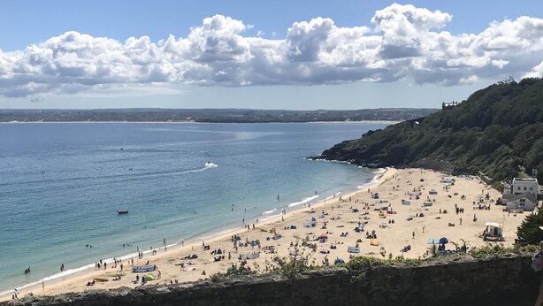 Una playa con cielo despejado, una orilla arenosa y una colina rocosa al fondo.