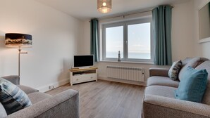 Una sala de estar con televisor sobre un mueble bajo, una lámpara de pie, un sofá y una ventana con cortinas.