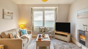 Ein Wohnzimmer mit einer Couch, einem Couchtisch, einem Fernseher, einem Kamin und einem großen Fenster mit Blick.