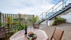 Eine Terrasse im Freien mit einem Tisch für zwei Personen, einer Weinflasche und einer Obstplatte.