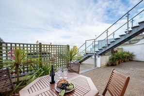Eine Terrasse im Freien mit einem Tisch für zwei Personen, einer Weinflasche und einer Obstplatte.