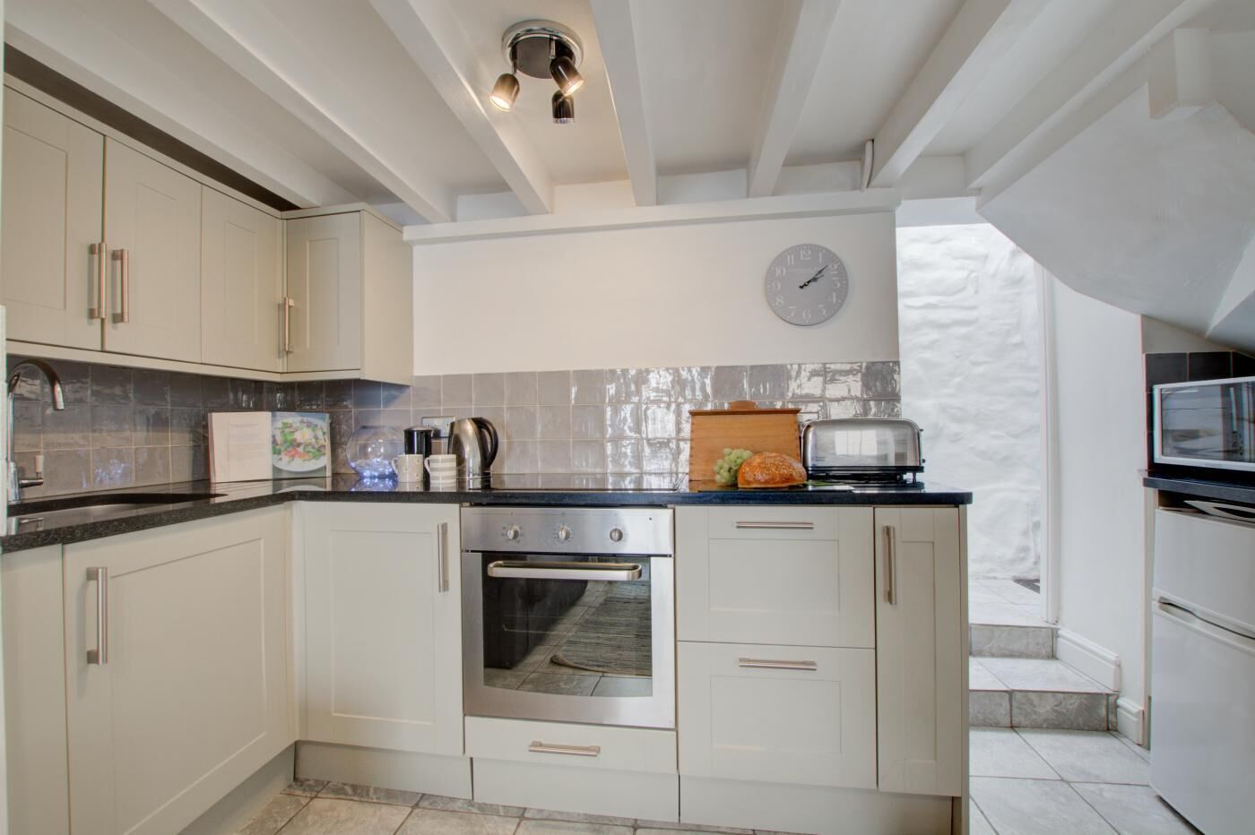 A modern kitchen with white cabinets, a built-in oven, a microwave, and a clock on the wall.