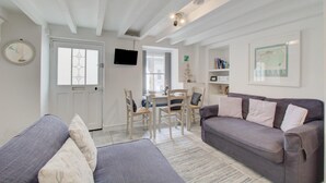 A living room with a grey sofa, a dining table with chairs, a TV mounted on the wall, and a bookshelf. - 2 Bed in St Ives (oc-stg019) (Saint Ives)