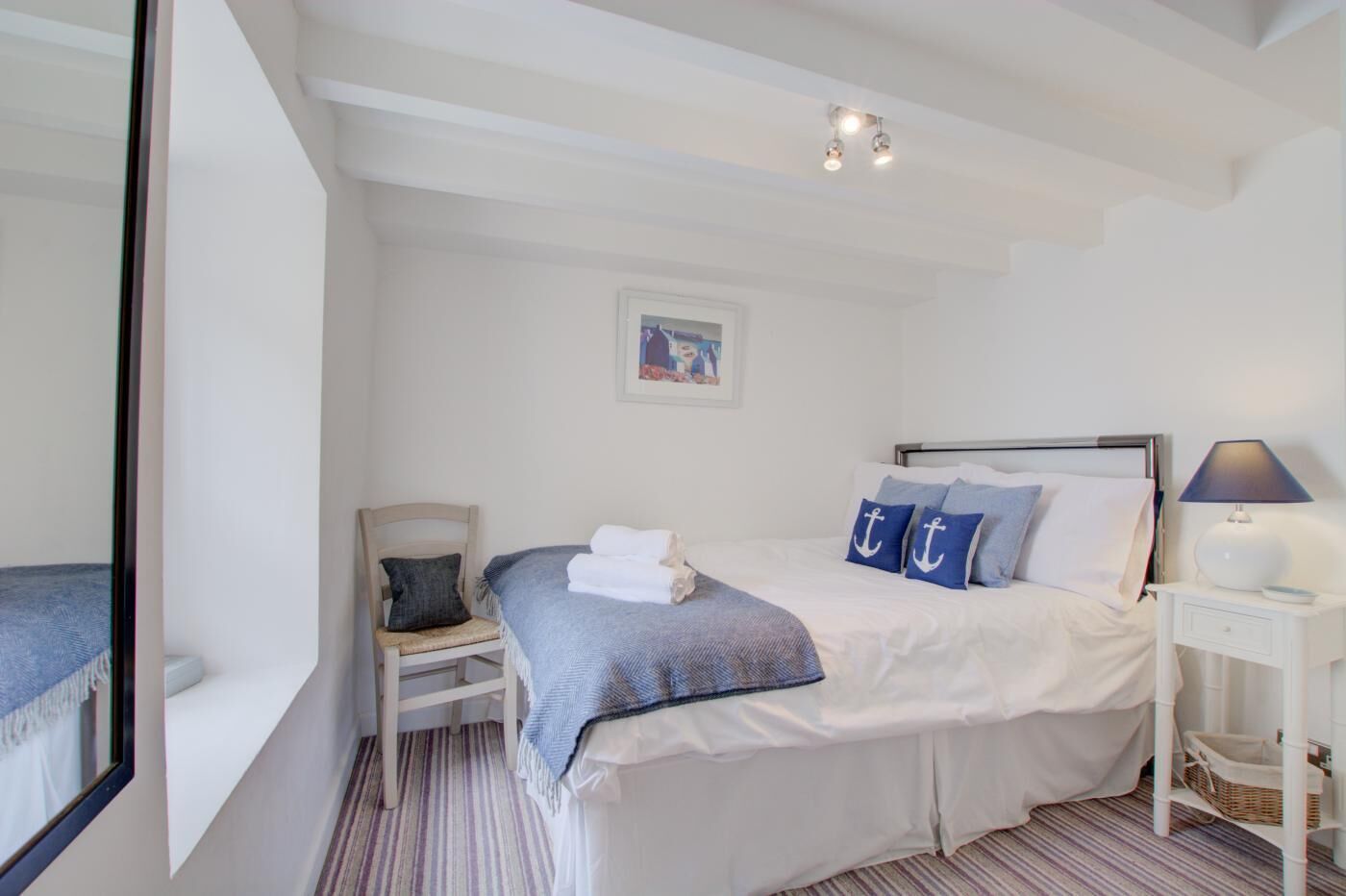 Een keurig opgemaakte slaapkamer met een bed, een stoel, een nachtkastje en een lamp.