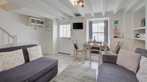 A living room with a sofa, a dining table with chairs, a television mounted on the wall, and a small Christmas tree. - 2 Bed in St Ives (oc-stg019) (Saint Ives)