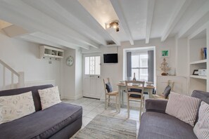 A living room with a sofa, a dining table with chairs, a television mounted on the wall, and a small Christmas tree. - 2 Bed in St Ives (oc-stg019) (Saint Ives)