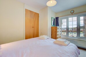 Une chambre à coucher comprenant un lit, une armoire en bois, une commode et une fenêtre donnant sur des bateaux et un port.