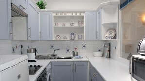 Cozinha compacta com armários cinzentos, forno embutido e micro-ondas.