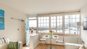 A room with a bay window, a dining table with chairs, a sofa, and a radiator. - 1 Bed in St Ives (oc-chyr01) (St Ives)
