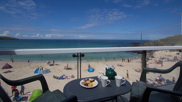Blick auf einen Strand von einem Balkon aus, mit einem Tisch, der mit Speisen und Getränken gedeckt ist, mit Blick auf einen belebten Strand.