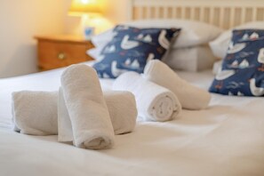 A neatly made bed with rolled white towels and a pillow with a nautical theme. - 2 Bed in St Ives (oc-shell) (St Ives)