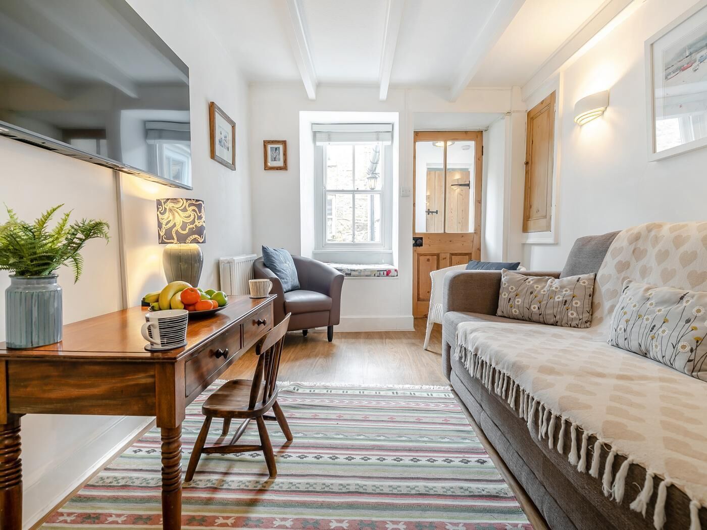 A cozy living room with a wooden coffee table, a comfortable sofa, a patterned rug, and a window with a view.