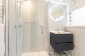 A modern bathroom with a glass-enclosed shower, a round mirror, and a dark-toned vanity. - 2 Bed in St Ives (oc-shell) (St Ives)