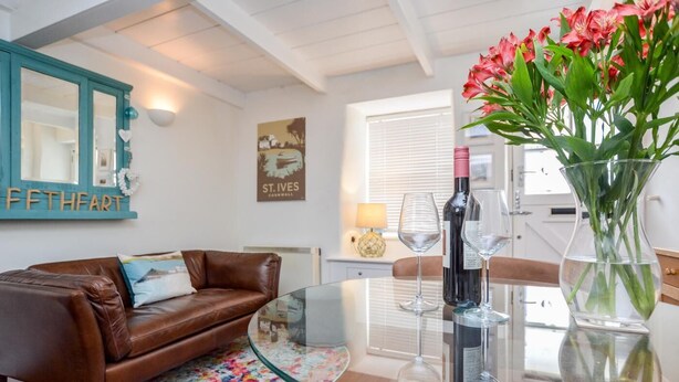 Un salon avec un canapé en cuir marron, une table basse en verre, un vase rempli de fleurs et une bouteille de vin.