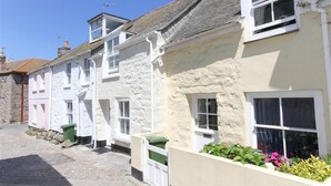 Une rue étroite bordée de maisons traditionnelles en pierre et en crépi, avec des fenêtres et des volets blancs.