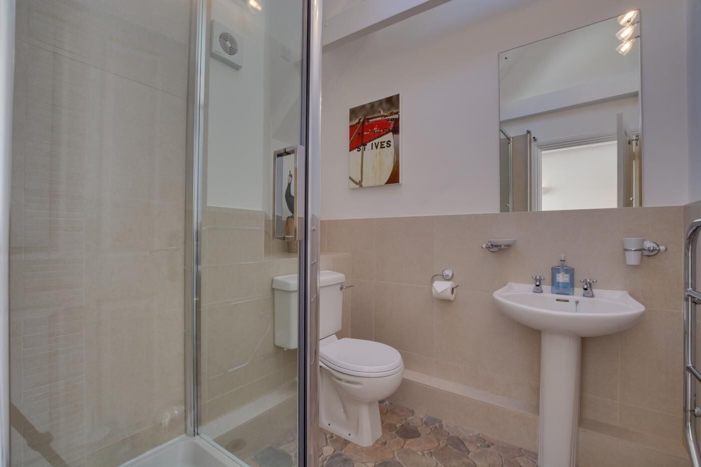 A bathroom with a glass shower enclosure, a toilet, a sink, and a mirror.
